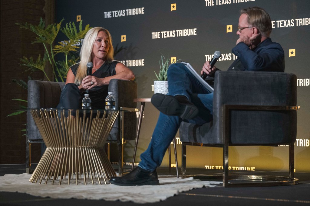 A panel discussion with a woman speaking into a microphone while seated next to a man holding a notebook, both positioned in front of a backdrop featuring 'The Texas Tribune.'