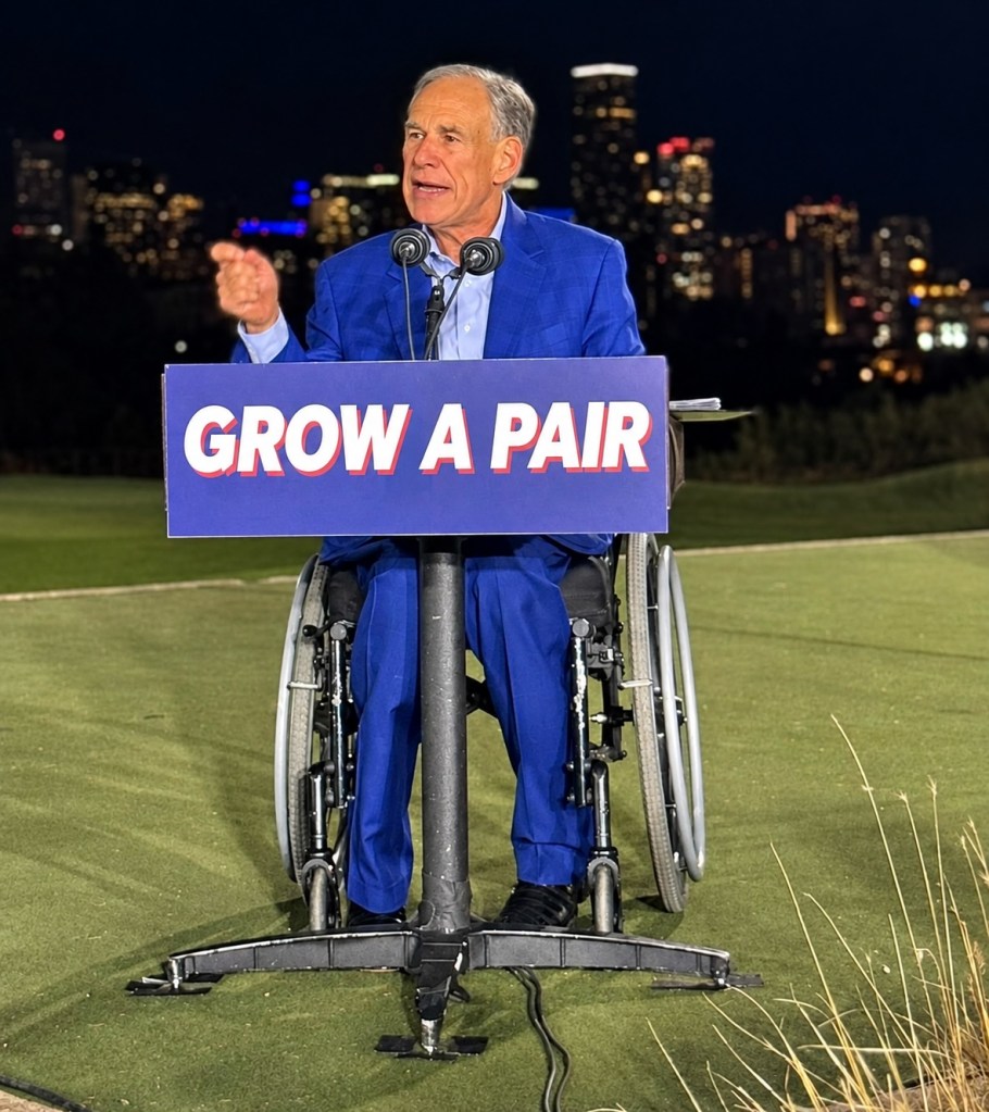 A man in a blue suit sitting in a wheelchair speaks at a podium with the words 'GROW A PAIR' against a city skyline at night.